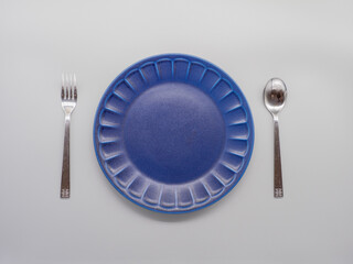 白い背景に置かれた紺色のお皿とカトラリー（フォーク及びスプーン）