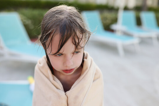 Wet frozen child by the pool, covered with a towel