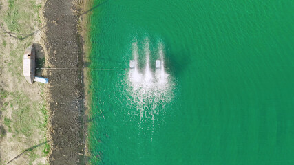 Aerial view of water turbines machine on lake, pond or river in farm field in industry factory. Power, sustainable green clean energy, and environment concept. Nature innovation.