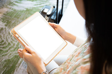 Mockup - blank screen tablet isolated with clipping. Happy Asian young woman tourist sitting on the bed.