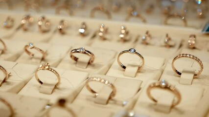 Rows of beautiful expensive fashionable gold rings behind the glass of a jewelry store window shine brightly with their diamonds. Shot in motion. Closeup