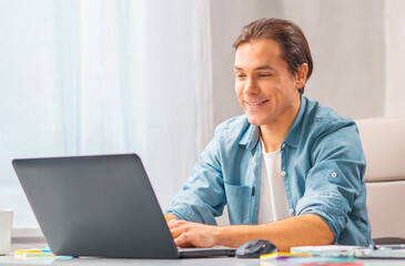 Young man works at a laptop computer. Freelancer, remote worker or student workplace. Distant work concept.