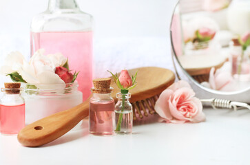 Herbal beauty treatment cosmetic product, fresh delicate pink rose flowers, bathroom shelf with skincare toiletries bottles, haircomb, mirror. Botanical spa body and hair care, soft pastel color