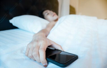 Young Asian woman lying on bed. Woman under white blanket with mobile phone. Wake up time.