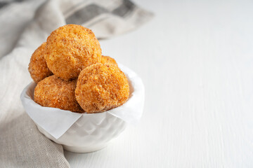 Italian homemade Arancini rice balls or croquettes stuffed, coated with bread crumbs and deep fried served in bowl as appetizer on white wooden background with textile towel. Image with copy space