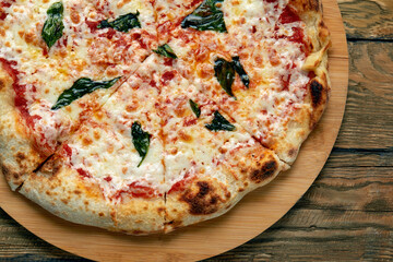 Uncut Italian pizza served with fresh basil leaf on Wooden board on dark texture background. Hot pizza with tomatoes and pesto sauce
