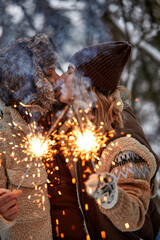 Couple Love Story in Snow Forest Kissing and Holding Sparklers. Couple in Winter Nature. Couple Celebrating. Valentine's day date.