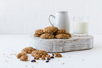 oatmeal biscuits on a white wooden podium with a glass of milk, a jug opposite a white brick wall....