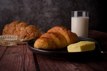 Delicious breakfast croissant with butter on a wooden table with glass milk.