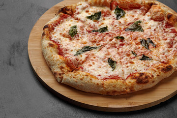 Uncut Italian pizza served with fresh basil leaf on Wooden board on dark texture background. Hot pizza with tomatoes and pesto sauce
