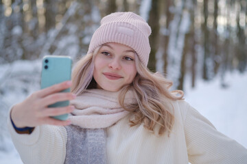 young beautiful woman takes a selfie on a smartphone camera in a snowy park