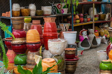 Several ceramic pots of different sizes and colors, next to ornamental plants and flowers inside a plant nursery.