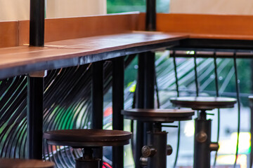 Fototapeta na wymiar A line of industrial stool with a rustic metal pipe and valve stands beyond a long brown hard wood table at cafe or coffee shop outdoor interior