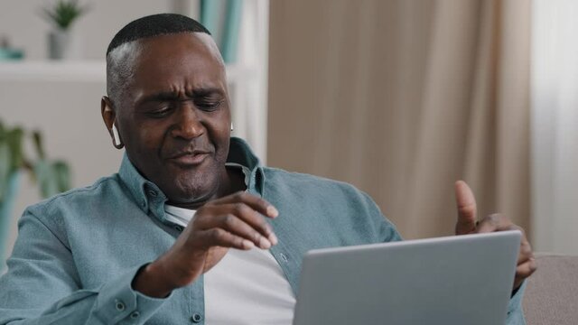 African american businessman freelancer distracted from work by laptop happy man sitting home on sofa listening to music in wireless headphonesenjoys favorite song dancing to energetic rhythm of audio