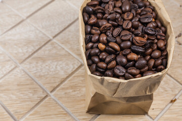Coffee beans in a brown paper bag on wooden background.