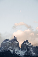 Part of the Torres del Paine mountains (peaks) against the cloudy sky Snow-capped peaks of mountains in an unusual shape against the sky with clouds and in the distance a small month. dust