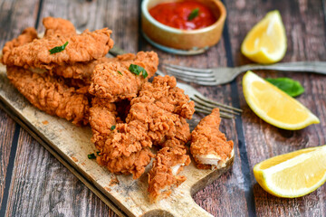 
 Crispy  deep fried   chicken strips and wedges potato. Breaded  with cornflakes chicken  breast fillets  with chilly peppers and fresh   basil on wooden rustic background