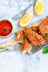 
 Crispy  deep fried   chicken strips and wedges potato. Breaded  with cornflakes chicken  breast fillets  with chilly peppers and fresh   basil on wooden rustic background