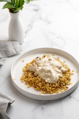 Bulgur with chicken and cream sauce. Dinner idea with bulgur porridge and chicken fillet. White background and white plate