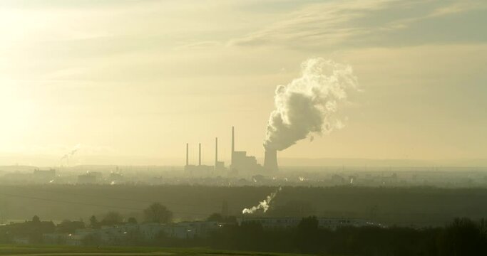 Time-lapse of a powerplant as it pushes out steam with clouds moving behind it in a hazy smoggy atmosphere.