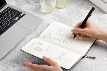 Hands writing in a notebook by pen, making notes. Desk with laptop. Remote work. Learning