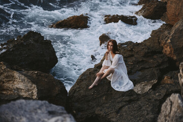 Fototapeta na wymiar barefoot woman in white dress sits on a stone with wet hair