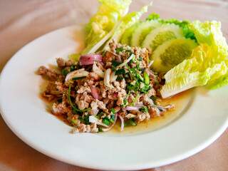 Thai food, spicy minced pork salad Larb Moo on white dish with spoon and fork on wooden background, close up