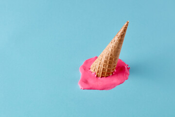 Dropped upside down ice cream cone with melting scoop on pastel blue floor. Minimalistic summer food