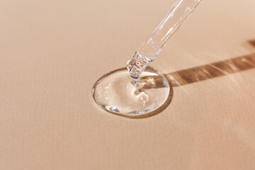 Hyaluronic acid in a glass pipette on a beige background. Transparent serum with beautiful texture...
