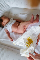 Close up on hand of unknown caucasian woman changing diapers with yellow faces dirty shit on her newborn baby - motherhood stinky poop challenge concept - obrazy, fototapety, plakaty