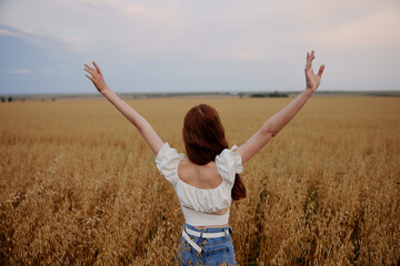 Fototapeta premium woman with raised up hands in the field admires the landscape back view