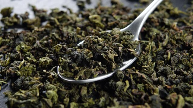 A spoonful of green dried oolong tea leaves on a black slate kitchen surface. Macro. Rotation
