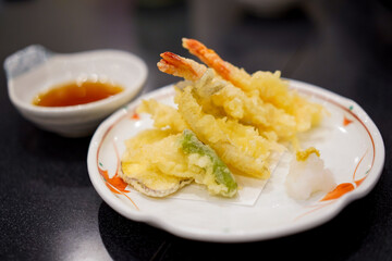 Tempura Shrimps and vagetable deep fried with soy sauce bowl in Japanese style on white plate and black table background.