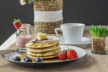 Pancakes served with butter, honey and fruirs served on a wooden table