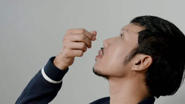 4K, Close Up Asian man's hands use a rapid antigen test kit to self-test the COVID-19 at home. A long cotton swab is inserted into the nose and internal nasal fluid sample for COVID-19 testing.