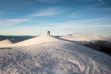 Beautiful landscape with snow-covered mountain slopes and the Monument Arch of Freedom at the main ridge of Balkan Mountains at Beklemeto pass, Bulgaria in winter morning