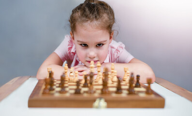 the girl looks at the chess pieces placed on the chessboard at home