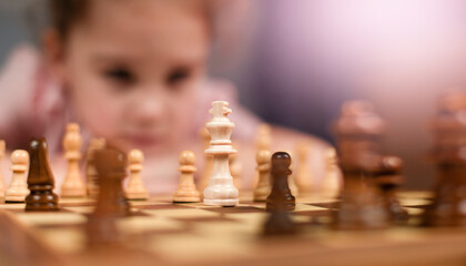 the girl looks at the chess pieces placed on the chessboard at home