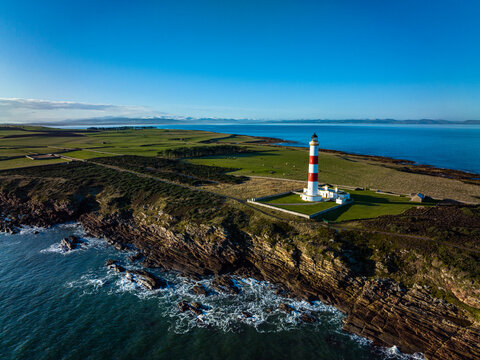 an aerial view of tarbat ness lighthouse on easter ross in the highlands of scotland near inverness showing blue sky and calm seas with the lighthouse dominating the scene and rocks
