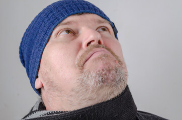 Portrait of a mature man looking up. A grown man wearing a blue hat against a light wall.