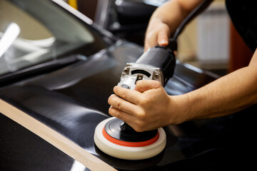 The concept of detailing and polishing cars. The hands of a professional car service worker, with an orbital polisher, polish the black luxury hood of a car in an auto repair shop. car polishing