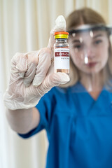 nurse with a transparent protective shield on her head and gloves holds a bottle of vaccine