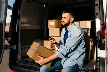 Thoughtful delivery man with package and smart phone sitting in van