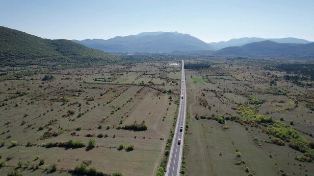Empty asphalt road on the plateau between green fields, aerial view. Flight over a long open road crossing deserted fields among mountain range. Scenic Highland way. Concept of Road trip on the car.