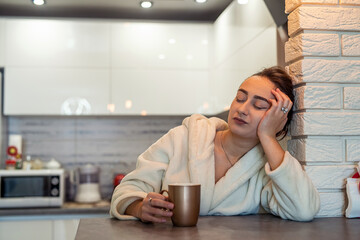 a young brunette in a bathrobe woke up sleepy in the middle of the night and drinking tea.