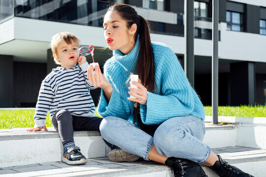 Playful mother blowing soap bubble by son in city
