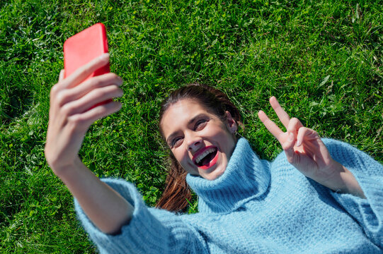 Cheerful woman taking selfie lying down on grass