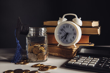 Savings for education concept. Glass jar with money and graduation hat near white alarm clock