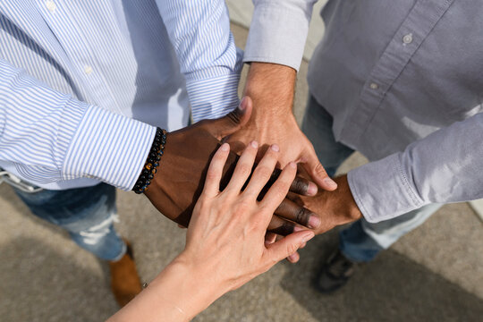 Multiracial friends doing stacking hands on footpath