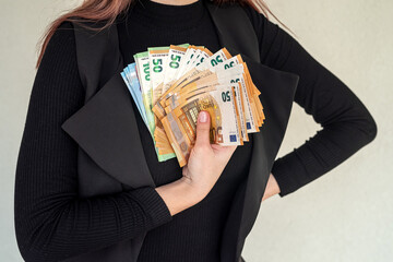 Beautiful young girl in a stylish black suit holds a large sum of new euros in his hands.